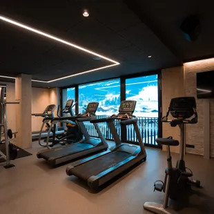 Fitnessraum in der Riederalm Modernes Fitnessstudio mit Cardiogeräten und Bergblick durch große Fenster